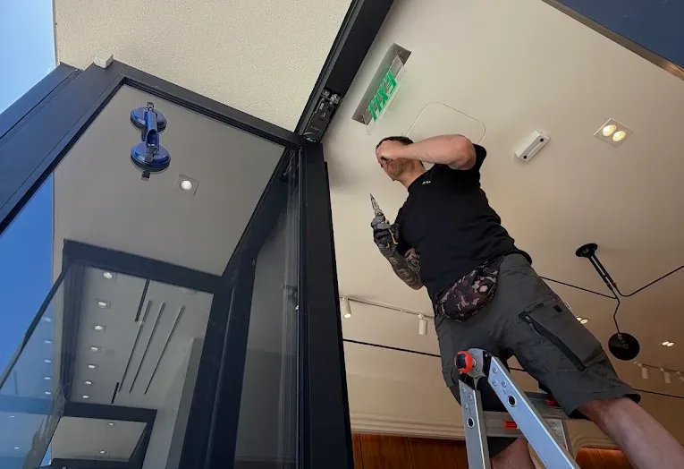 Technician working from a ladder at a commercial entrance.