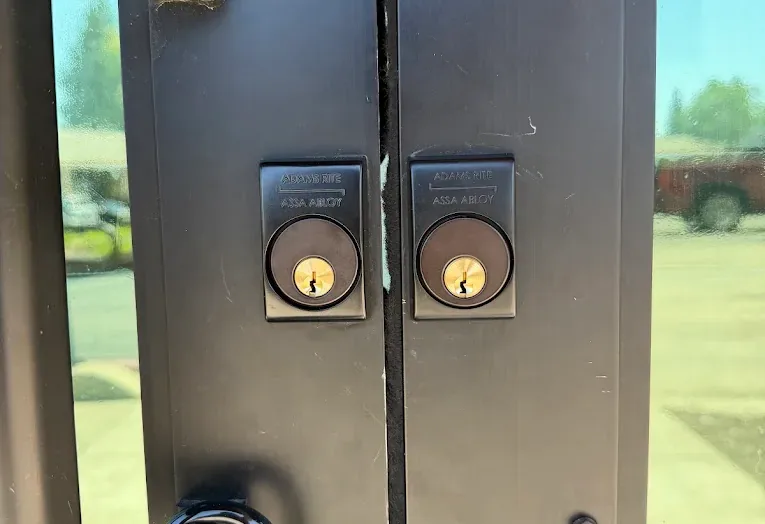 Two lock cylinders on a metal commercial double door.