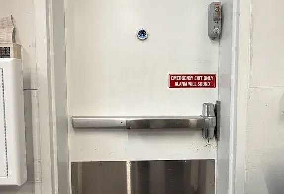 Steel exit door with a horizontal panic bar and safety label.