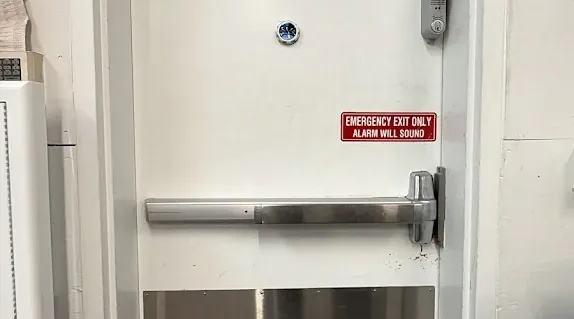 Steel exit door with a horizontal panic bar and safety label.