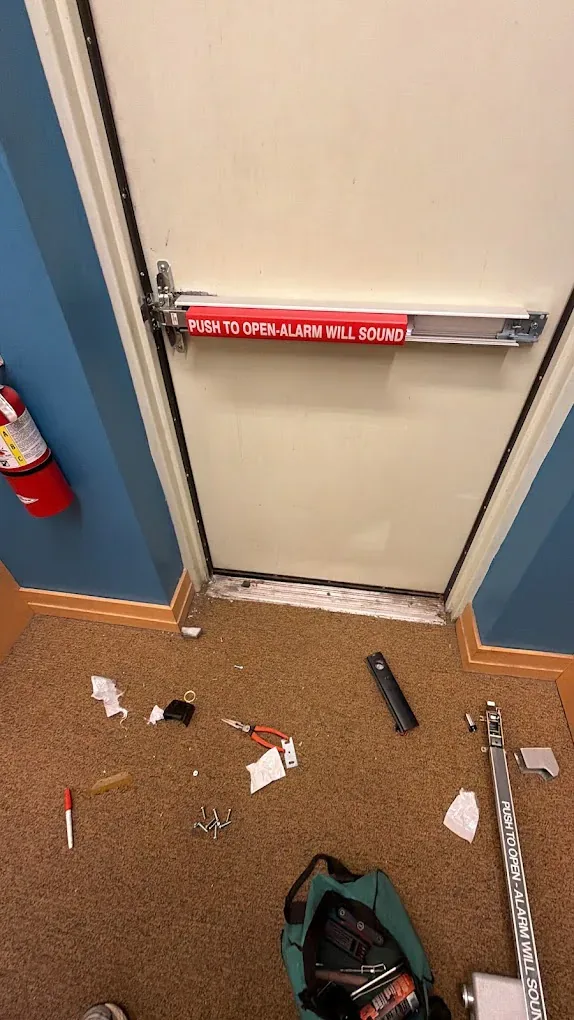 Panic bar parts and locksmith tools laid out beside a commercial exit door during repair