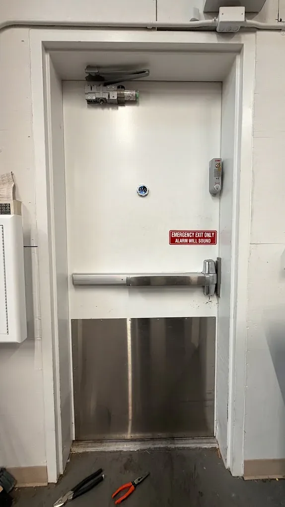 Steel exit door with a horizontal panic bar and safety label.