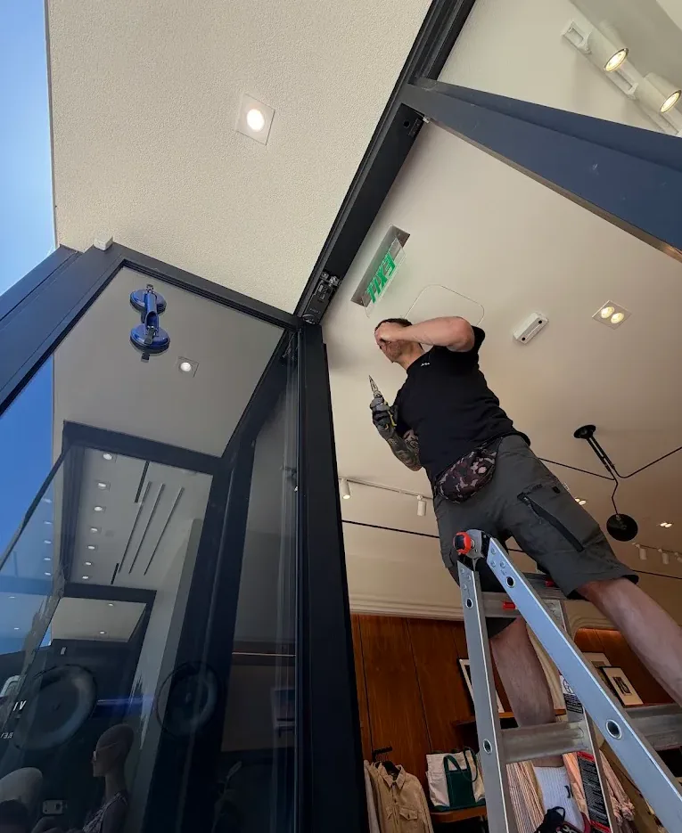 Technician working from a ladder at a commercial entrance